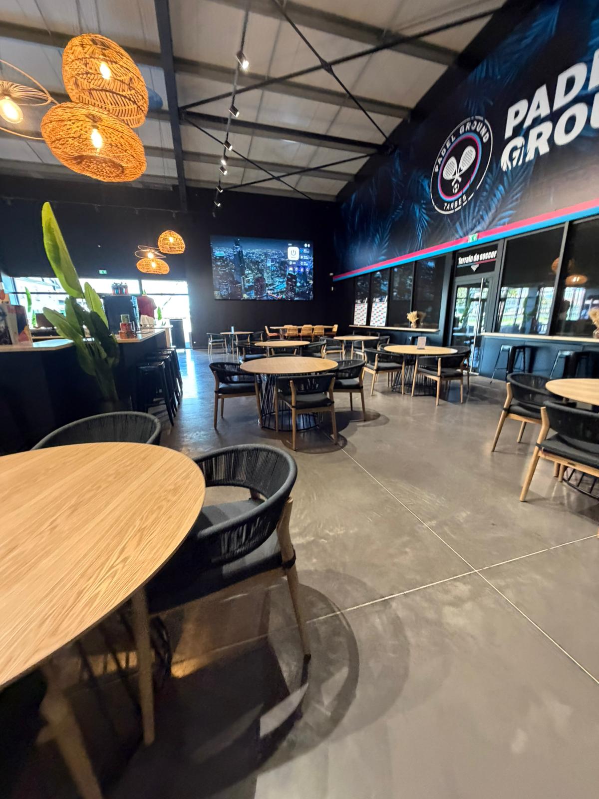 Padel Ground Tarbes — seating toward branded wall and TV